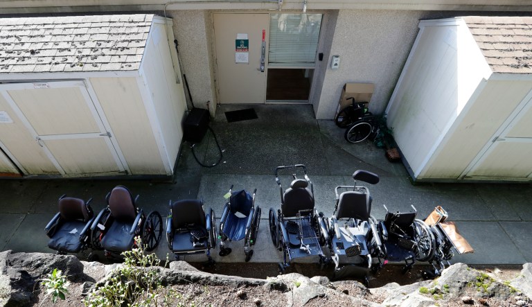 A line of wheelchairs sit outside a back door at the Life Care Center, where at least 30 coronavirus deaths have been linked to the facility, Wednesday, March 18, 2020, in Kirkland, Wash. Staff members who worked while sick at multiple long-term care facilities contributed to the spread of COVID-19 among vulnerable elderly in the Seattle area, federal health officials said Wednesday.