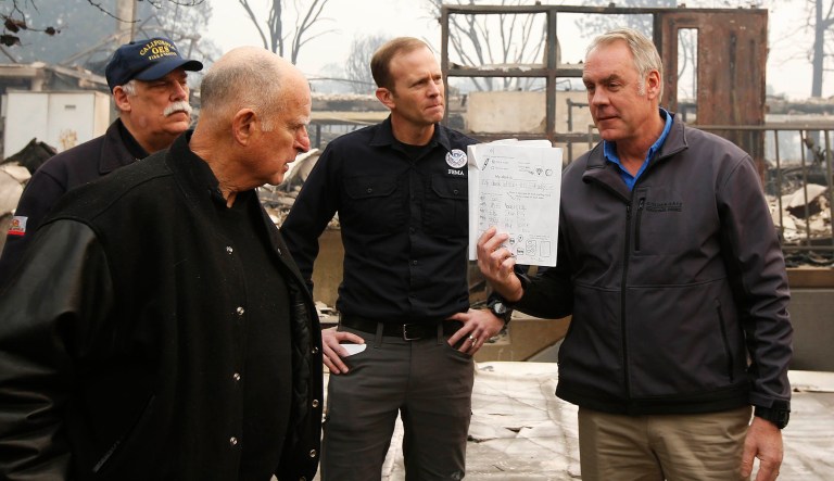 California Gov. Jerry Brown, second from left, looks at a students work book displayed by Interior Secretary Ryan Zinke, that was found during a tour of the fire ravaged Paradise Elementary School Wednesday, Nov. 14, 2018, in Paradise, Calif. The school is among the thousands of homes and businesses destroyed along with dozens of lives lost when the fire burned through the area last week.