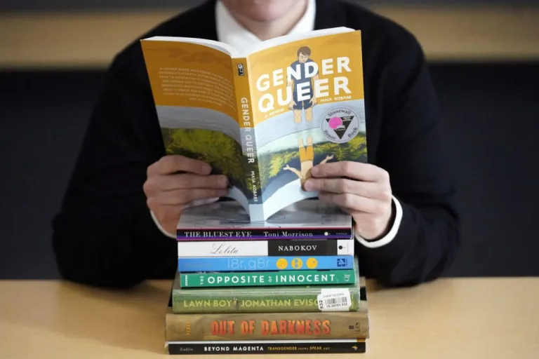 Amanda Darrow, director of youth, family and education programs at the Utah Pride Center, poses with books (showing her neck down minus her face) that have been the subject of complaints from parents on Dec. 16, 2021, in Salt Lake City. The nationwide surge in book banning continues. The American Library Association reported Wednesday, Sept. 20, 2023, that challenges to books in schools and public libraries will likely reach record highs in 2023, topping what had been a record pace in 2022. (AP Photo/Rick Bowmer, File)