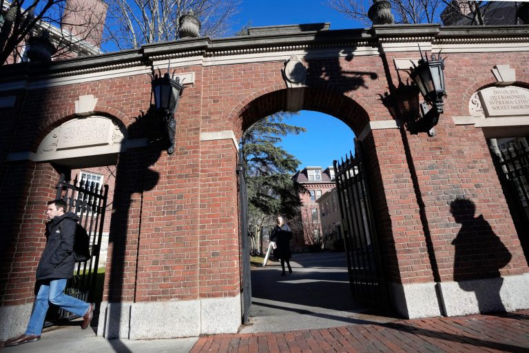 Passers-by walk near an entrance to Harvard University, Tuesday, Dec. 12, 2023, in Cambridge, Massachusetts. Harvard President Claudine Gay will remain leader of the prestigious Ivy League school following her comments last week at a congressional hearing on antisemitism, the university's highest governing body announced Tuesday. 