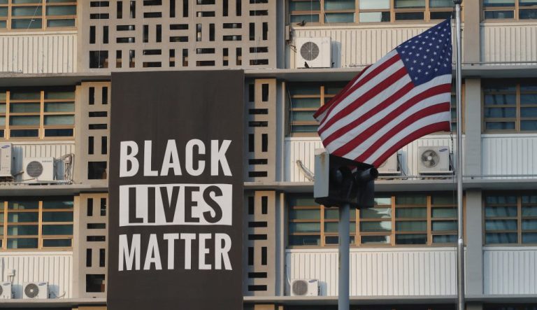 Black Lives Matter poster on a school building with an American flag waving outside.