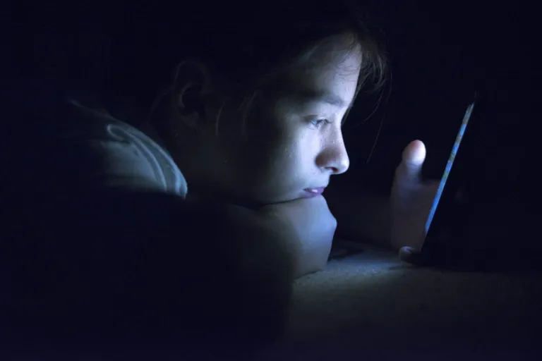 Teenager sending email from smartphone in her bed, typing message on smartphone.
