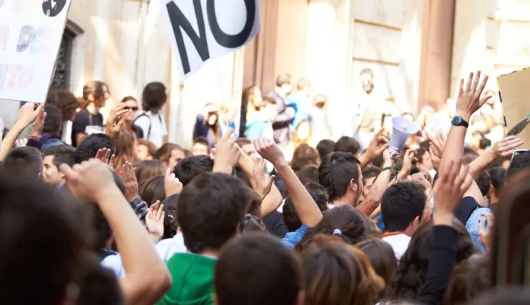 A labor union strike is seen with heads everywhere and arms up in protest with a sign donning a big NO in sharpie.