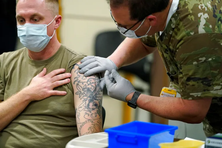Staff Sgt. Travis Snyder, left, receives the first dose of the Pfizer COVID-19 vaccine given at Madigan Army Medical Center at Joint Base Lewis-McChord in Washington state, Dec. 16, 2020, south of Seattle. U.S. military forces around the world will no longer be required to get the COVID-19 vaccine. The mandate was lifted under an $858 billion defense spending bill passed by Congress and signed into law by former President Joe Biden.