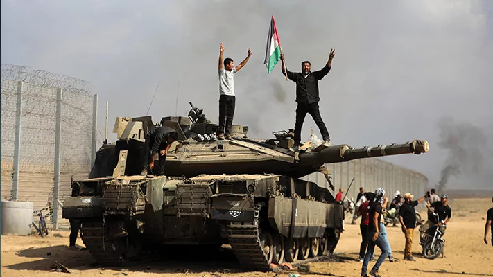 Palestinians wave their national flag and celebrate by a destroyed Israeli tank.