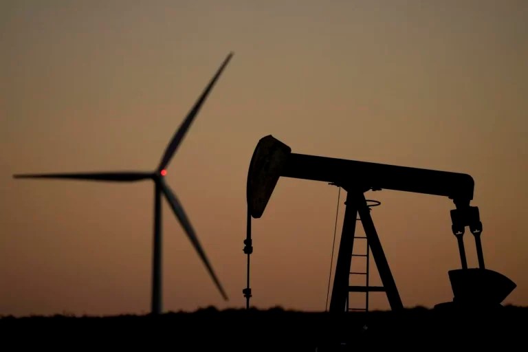 A pumpjack operates in the foreground while a wind turbine at the Buckeye Wind Energy wind farm rises in the distance, Monday, Sept. 30, 2024, near Hays, Kansas.
