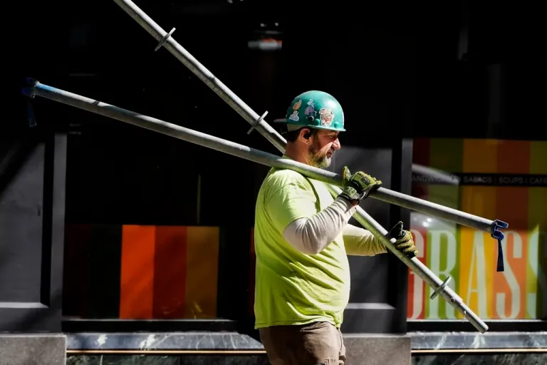 A construction worker carries scaffolding parts.