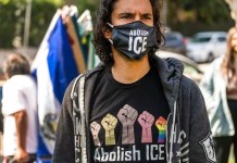 Activist Adam de Monet wears an "Abolish ICE" T-shirt and face mask as he participates in the "Reunite Our Families Now!'' rally to protest continued deportations, demanding family and children reunifications in Los Angeles Saturday, March 6, 2021. President Joe Biden's administration is instructing long-term facilities that hold immigrant children to lift capacity restrictions enacted during the coronavirus pandemic to open up much-needed beds in a system facing sharply increasing needs. Biden ended a practice under former President Donald Trump of expelling unaccompanied children under a public-health declaration enacted during the pandemic, though his administration continues to expel immigrant families and adults. (AP Photo/Damian Dovarganes)