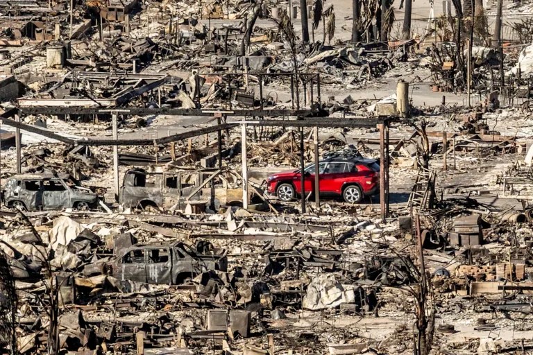 A car drives past homes and vehicles destroyed by the Palisades fire at the Pacific Palisades Bowl Mobile Estates, Sunday, Jan. 12, 2025, in Los Angeles.