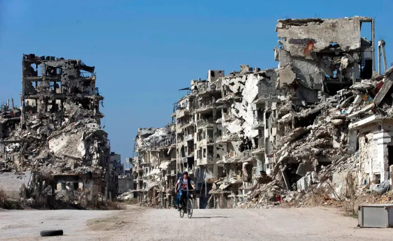In this Feb. 26, 2016, file photo, a Syrian boy rides a bicycle through a devastated part of the old city of Homs, Syria.