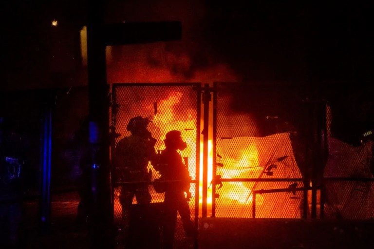 Federal officers guard the Mark O. Hatfield U.S. Courthouse as a fire lit by protesters burns on the other side of a perimeter fence Saturday, July 25, 2020, in Portland, Ore. (AP Photo/Noah Berger)