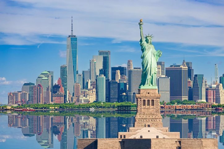 Statue of Liberty and New York City Skyline with Manhattan Financial District, Battery Park, Water of New York Harbor, World Trade Center, Empire State Building, Governors island and Blue Sky with Puffy Clouds.