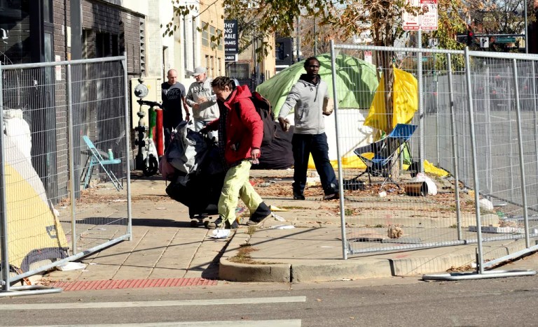 A homeless man moves his belongings during a sweep of an encampment in downtown Denver on Tuesday, Oct. 31, 2023. Crews erected fencing along several blocks near a post office, and police ordered campers to leave. More cities across the U.S. are cracking down on homeless tent encampments that have grown more visible and become unsafe.