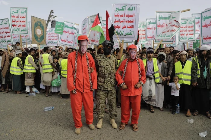 Houthi supporters perform an officer stands between two individuals wearing red prison uniforms and face masks depicting Israeli Prime Minister Benjamin Netanyahu, left, and U.S. President Donald Trump, during a weekly anti-U.S. and anti-Israel rally in Sanaa, Yemen, Friday, May 9, 2025.