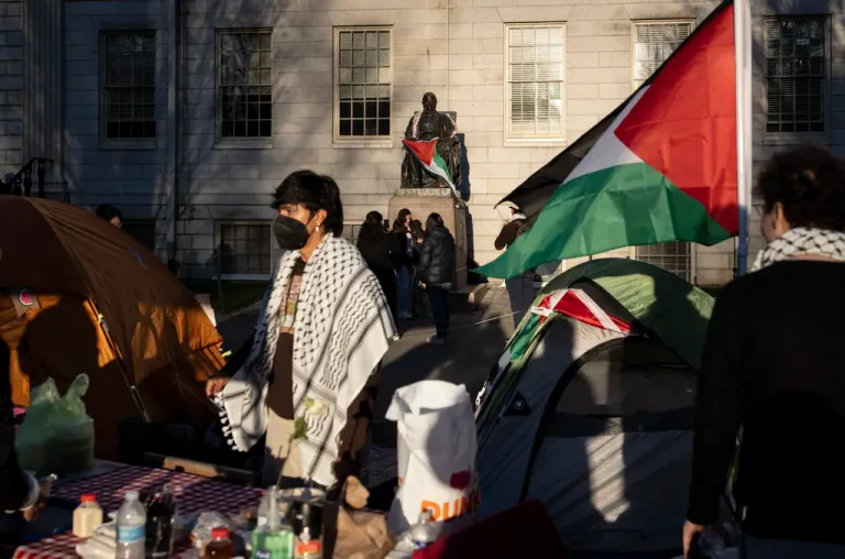 A student protester stands in front of the statue of John Harvard, the first major benefactor of Harvard College, draped in the Palestinian flag, at an encampment of students protesting against the war in Gaza, at Harvard University in Cambridge, Massachusetts, April 25, 2024.