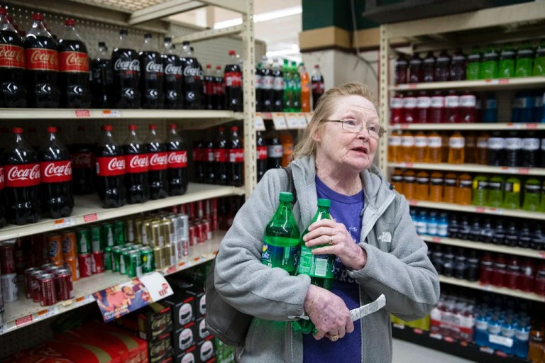 In this March 16, 2017 photo, Margaret Atkinson speaks during an interview as she shops for soda at the IGA supermarket in the Port Richmond neighborhood of Philadelphia. Less than three months into Philadelphia's new tax on sweetened drinks, the stakes have escalated: Beverage makers say the measure is hurting sales so much they need to cut jobs, while city officials say the moves are a ploy to get the tax struck down. Atkinson said she has switched to generic brands and is asking a nephew in the suburbs to pick up soda for her. She's also drinking more homemade iced tea and bottled water with flavor packets.