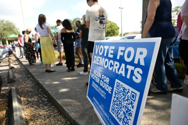 A Vote For Democrats sign is viewed as people stand in line to vote in the general election outside of an early voting location, Wednesday, Oct. 30, 2024, in Orlando, Fla.
