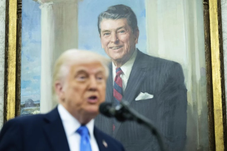 With a painting of former President Ronald Reagan behind him, President Donald Trump speaks into a microphone.