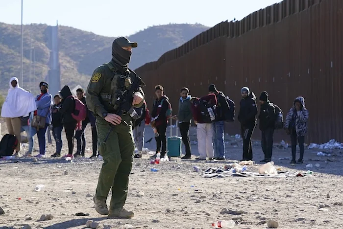 A member of Customs and Border Protection walks past a group of migrants.
