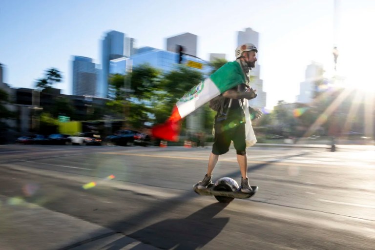 A person wearing a Mexican flag rides a scooter while picking up trash during a demonstration, Sunday, June 15, 2025, in Los Angeles.