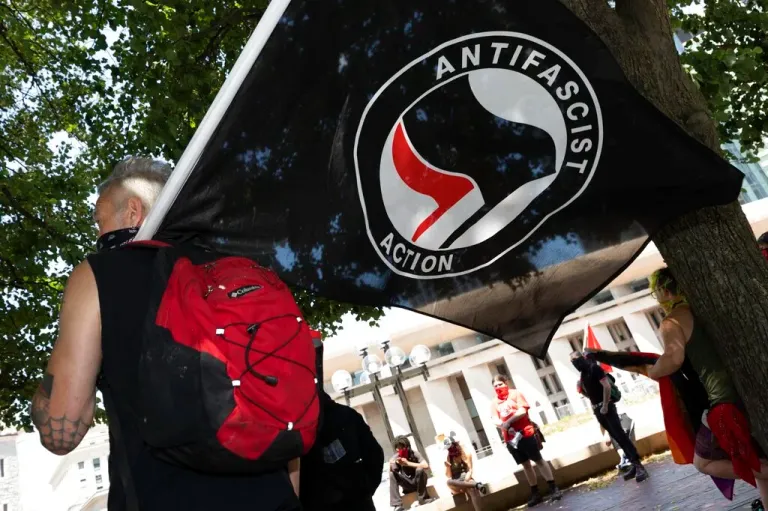 An antifascist protester holds a flag on the Christian Science Plaza, Saturday, July 11, 2020, in Boston. Dozens of demonstrators gathered in counter-protest against an anticipated rally by a right-wing group that never materialized.