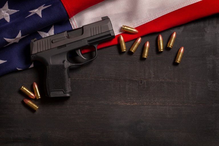 Black pistol and bullets with an American flag on a black wood painted background.