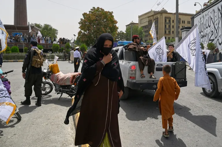 A woman wearing a face mask walks quickly through crowds of Taliban fighters and supporters during celebrations marking the fourth anniversary of the U.S. withdrawal and the start of Taliban rule in Kabul, Afghanistan, Friday, Aug. 15, 2025.
