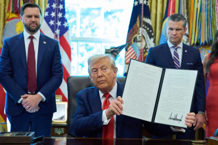 President Donald Trump holds up an executive order on cashless bail as Vice President JD Vance, left, and Defense Secretary Pete Hegseth look on, in the Oval Office of the White House, Monday, Aug. 25, 2025, in Washington.