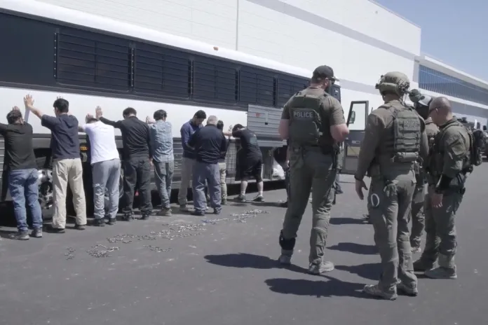This image from video provided by U.S. Immigration and Customs Enforcement via DVIDS shows manufacturing plant employees waiting to have their legs shackled at the Hyundai Motor Group’s electric vehicle plant, Thursday, Sept. 4, 2025, in Ellabell, Georgia.