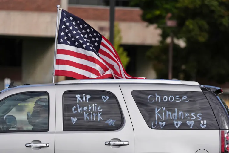 A vehicle marked with messages on its windows in tribute to Turning Point USA CEO and co-founder Charlie Kirk and carrying an American flag.