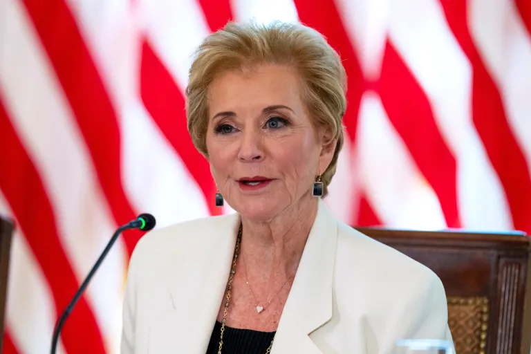 Linda McMahon, seated, speaks into a microphone with American flags in the background.