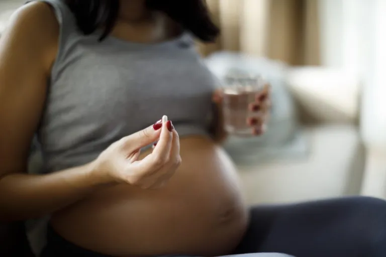 A pregnant woman holding a pill and a glass of water.