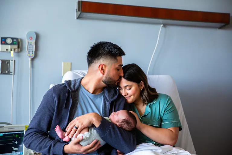 A young family consisting of a hispanic father and mother and their newborn baby boy in the hospital with grandparents, a nurse, and a pediatrician.