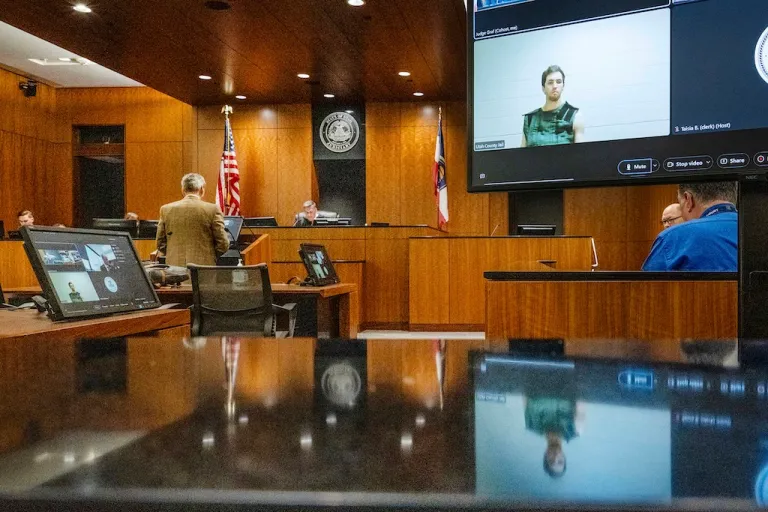 Defense attorney Greg Skordas, left, speaks before Judge Tony Graf, background, in Provo, Utah, as Tyler Robinson, in monitor at right, accused of fatally shooting Charlie Kirk, attends the court hearing virtually from prison.