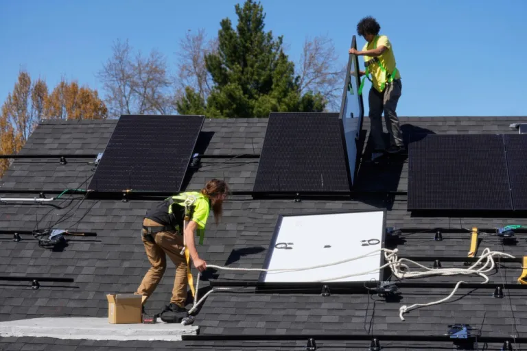 Two men installing solar panels on a house's roof.