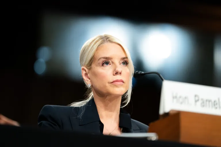 Pam Bondi sits at a desk behind a microphone