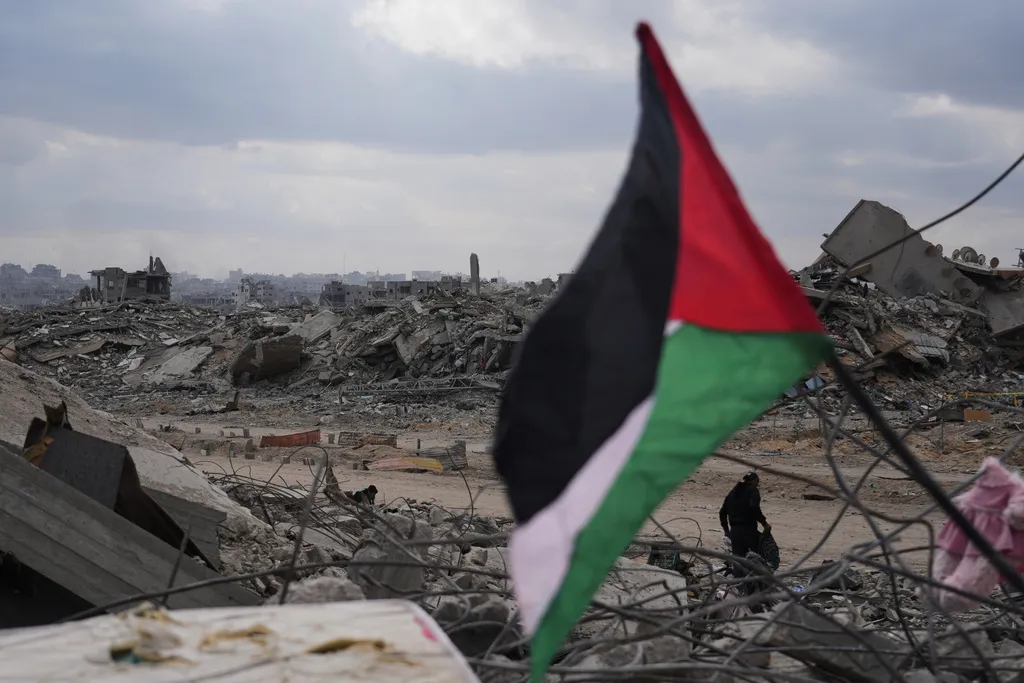 A displaced man walks past a Palestinian flag placed over the rubble of destroyed buildings in Gaza City, Sunday, Oct. 12, 2025, after Israel and Hamas agreed to a temporary pause in their war and the release of the remaining hostages.