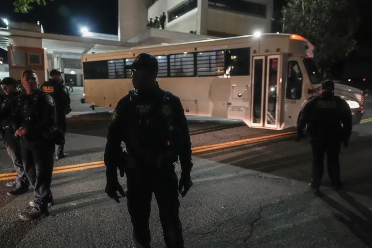 Law enforcement officers line the road outside an Immigration and Customs Enforcement facility as a bus leaves with passengers.