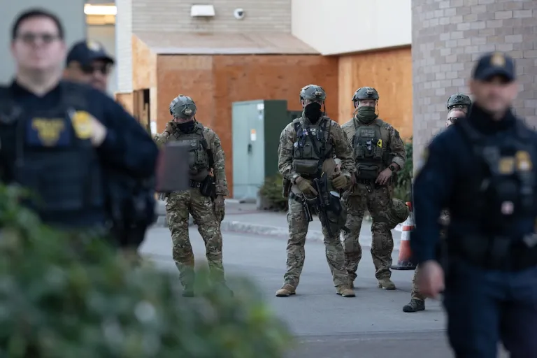 Law enforcement officers watch from a United States Immigration and Customs Enforcement (ICE) facility on Tuesday, Oct. 21, 2025, in Portland, Ore. (AP Photo/Jenny Kane)