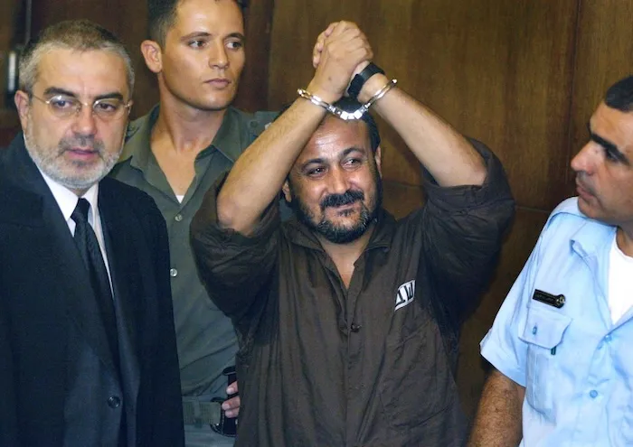Marwan Barghouti, center, raises his handcuffed hands in the air on the opening day of his trial in Tel Aviv, Israel, Aug. 14, 2002. (AP Photo/Brennan Linsley, File).