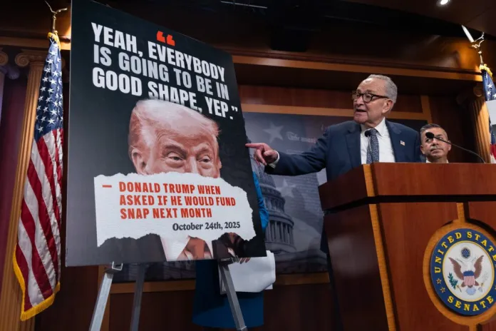 Senate Minority Leader Chuck Schumer (D-NY), left, flanked by Sen. Ben Ray Lujan (D-NM), right, points to a poster during a press conference.