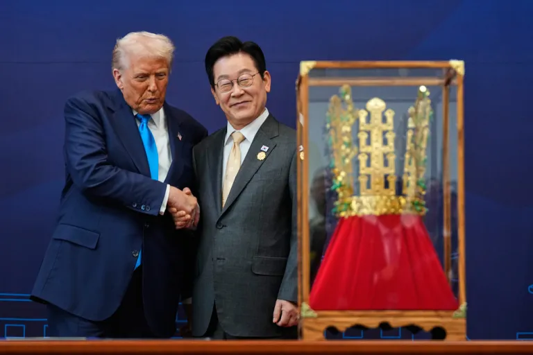 Donald Trump shakes hands with Korean President Lee Jae Myung in front his gold crown gift.