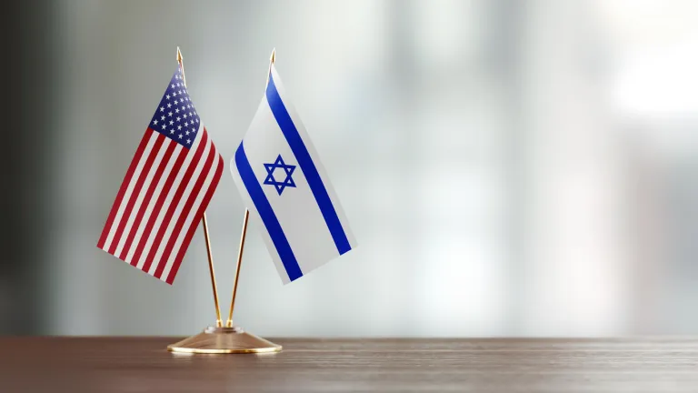 American and Israeli flag pair on desk over defocused background.