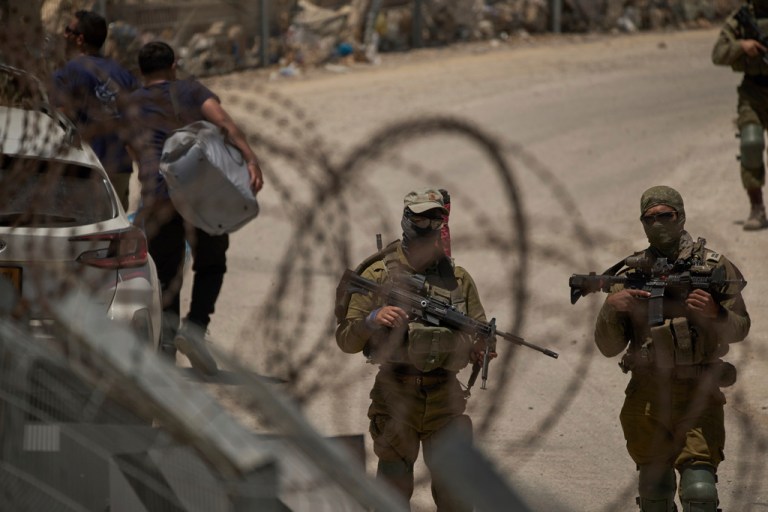Israeli soldiers stand guard as Syrian Druze people cross back into Syria at the Israeli-Syrian border.