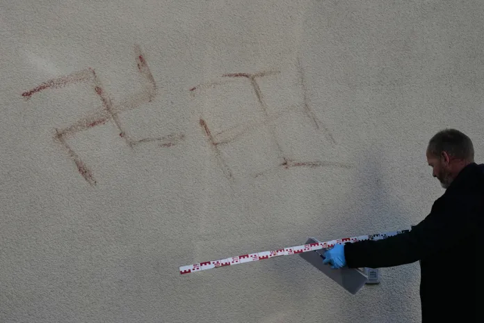 Criminal experts measure swatsikas at a house in Hanau, Germany, Thursday, Nov. 6, 2025, the day after a a person painted with blood swastikas on cars and houses.