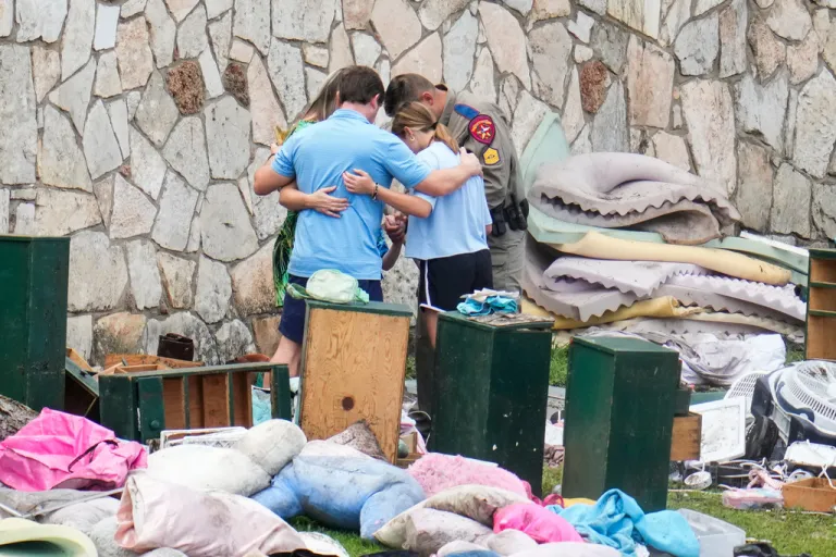 FILE - An officer prays with a family as they pick up items at Camp Mystic in Hunt, Texas, July 9, 2025. (AP Photo/Ashley Landis, File)