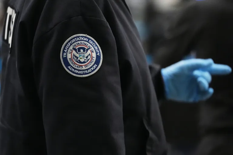 A TSA employee wears a jacket with the TSA and Department of Homeland Security logo.