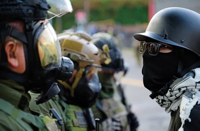 A masked and helmet-clad protester confronts federal agents outside the U.S. Immigration and Customs Enforcement building in Portland, Oregon, Oct. 4, 2025.(Mathieu Lewis-Rolland / Sipa USA / Newscom)