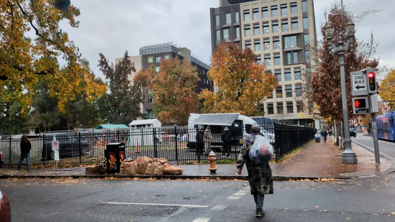 Man holding garbage bag walks through city.