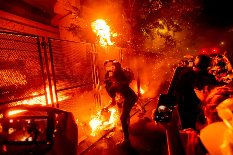 Protesters throw flaming debris over a fence.